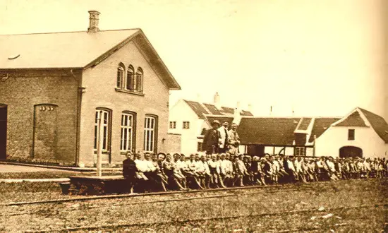 Billede af cirka 100 drenge på Knudshoved Stations perron. Til venstre stationsbygningen, længere tilbage opsynsmandens bolig.