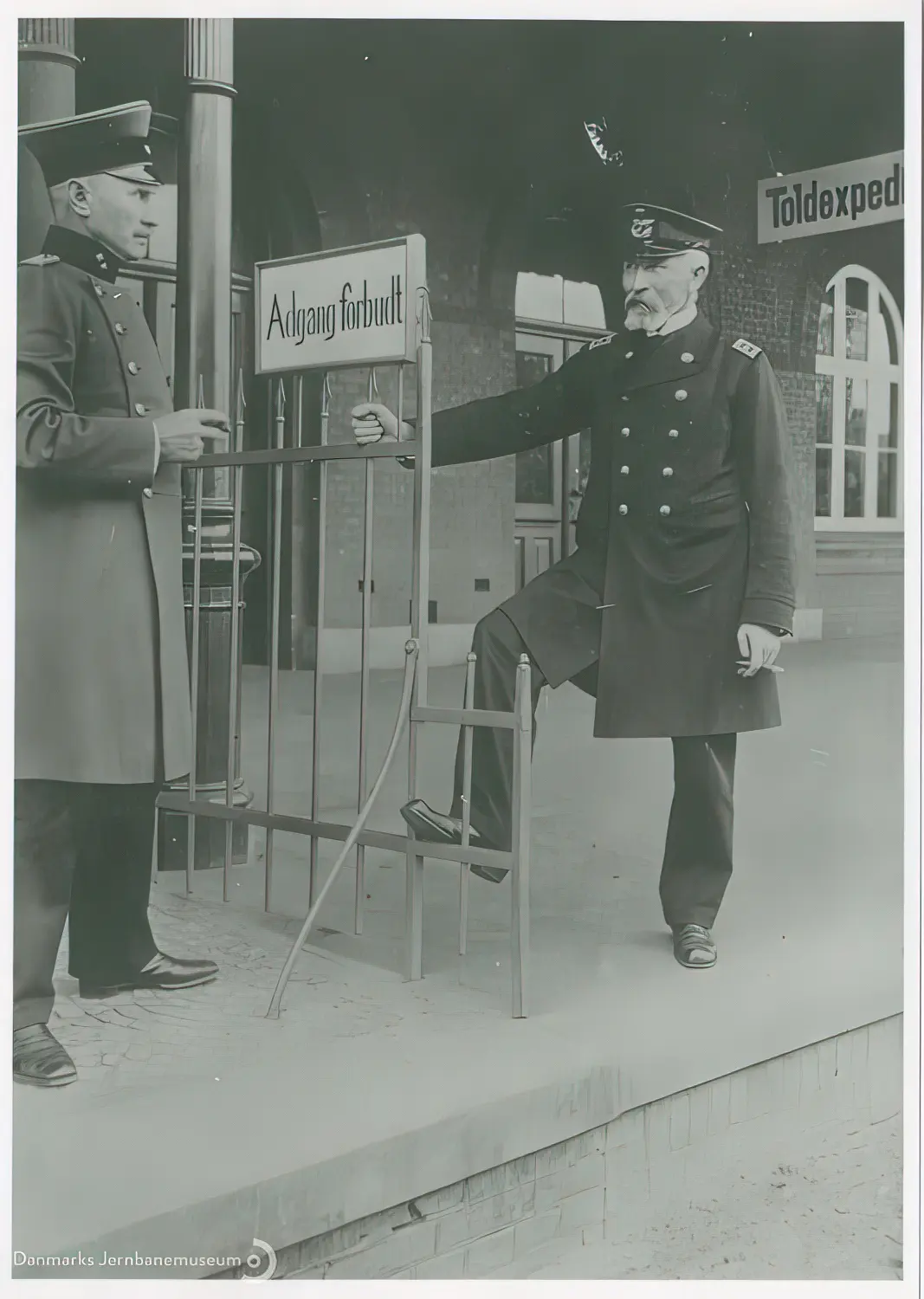 Billede af bahnhofsvorsteher Johan Friedrich Wilhelm Ehlers og stationsforstander Jens Jensen Høgdal i en cigarpassiar på tværs af perronens grænsestakit på Vedsted-Hvidding Station.